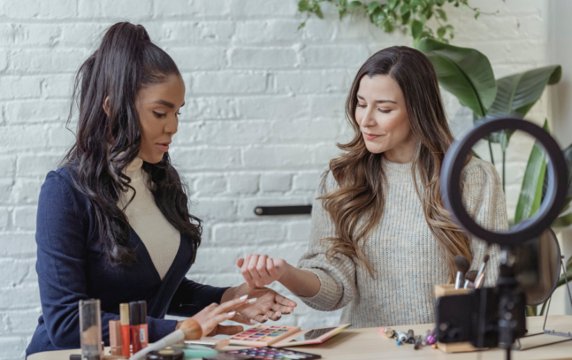 Two women discussing makeup products in a well-lit workspace, ideal for UGC content creation and beauty influencer work.